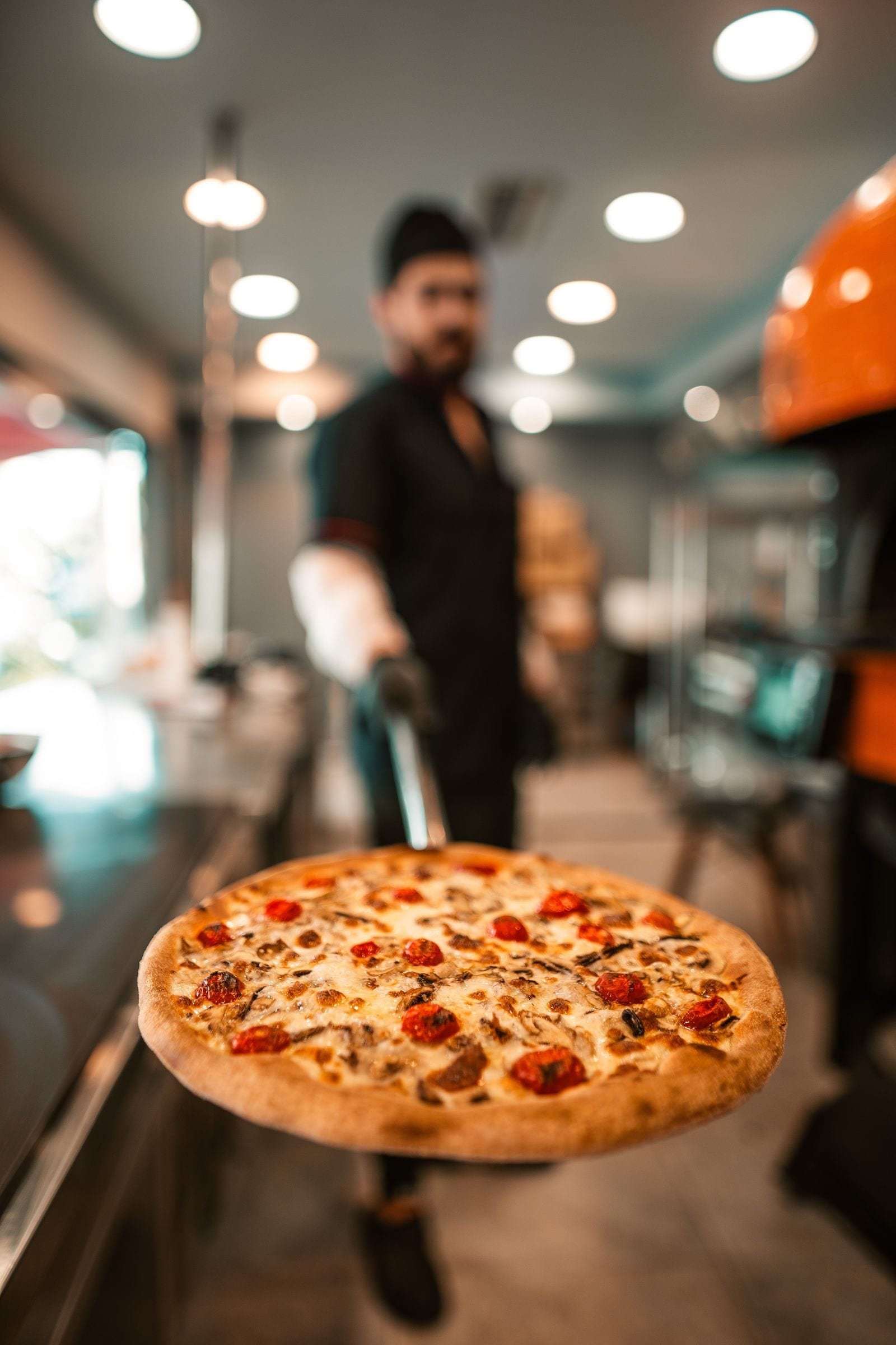 A chef pulling a fresh pizza out of a commercial pizza oven on a peel