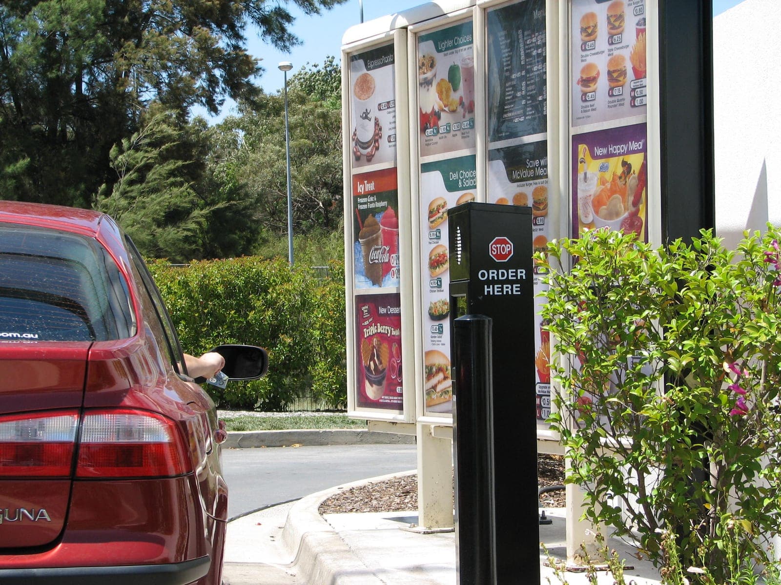A car ordering at a McDonald's drive-thru menu board with an Order Here sign