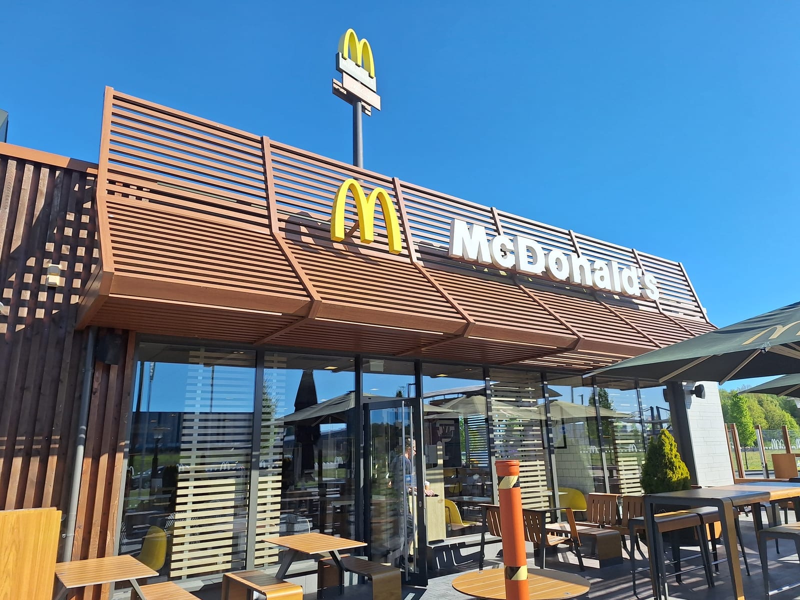 A McDonald's restaurant exterior with golden arches signage on a sunny day, outdoor seating in the foreground