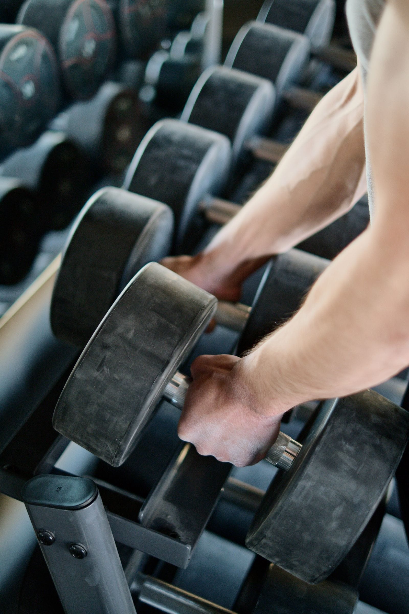 A gym member selecting dumbbells from a weight rack