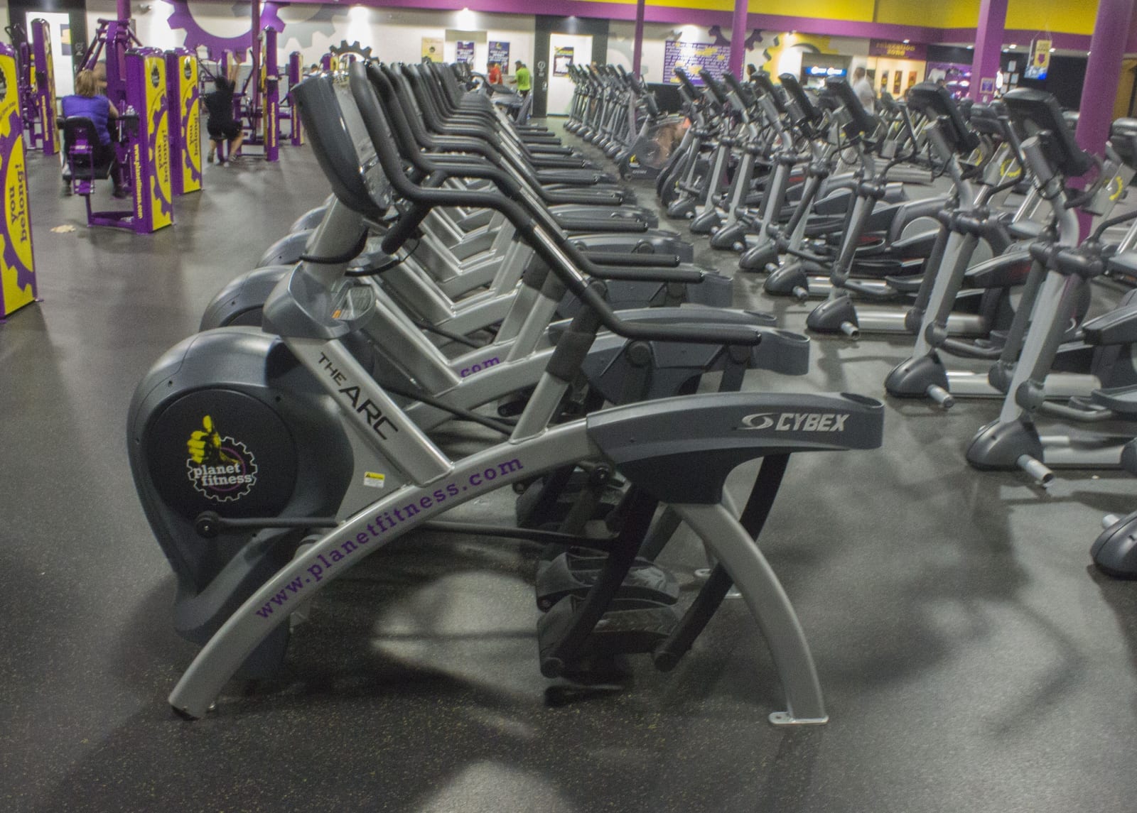 A row of Cybex Arc Trainer cardio machines on the gym floor at a Planet Fitness location