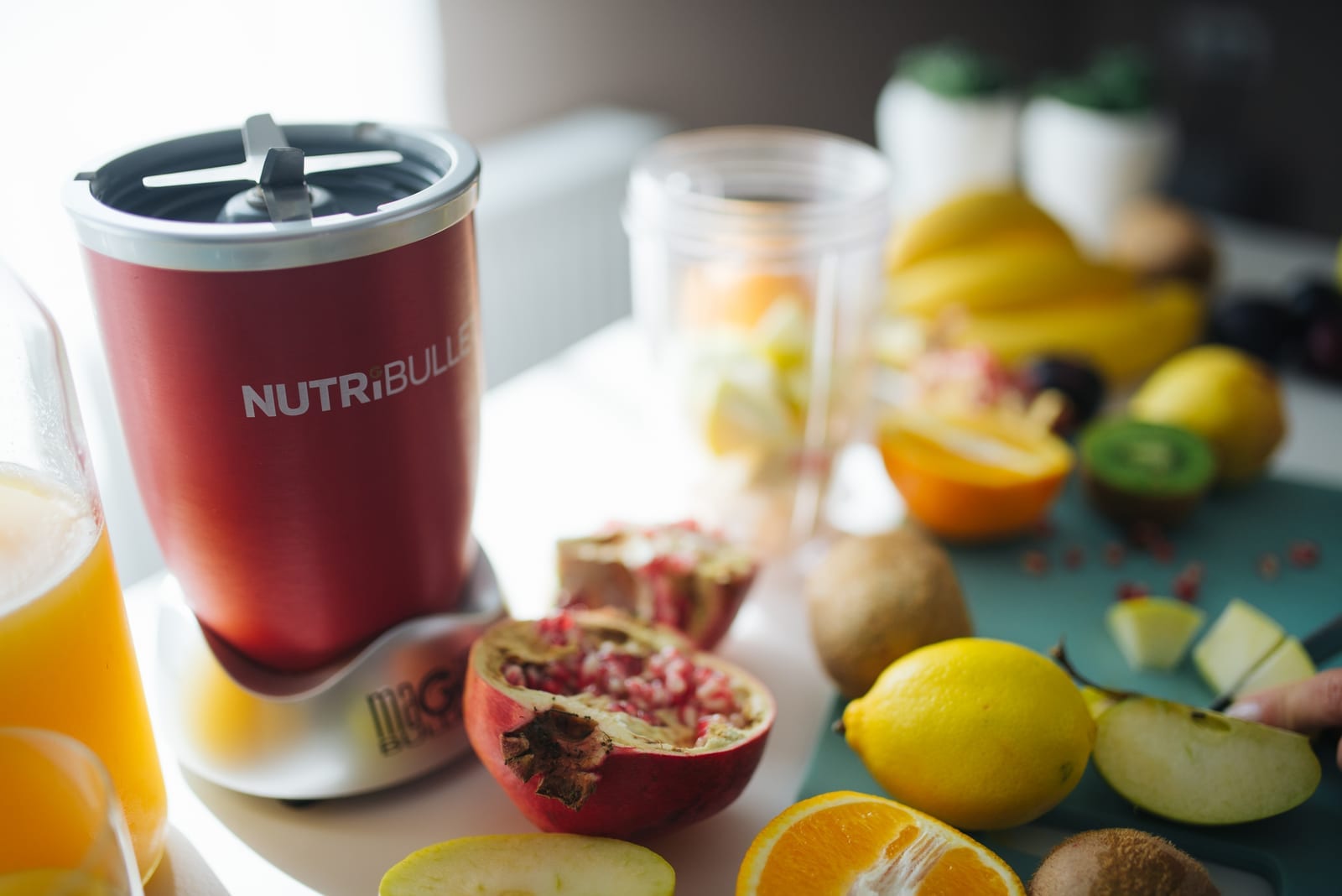 Fresh fruit and a countertop blender arranged for smoothie preparation, including pomegranate, kiwi, banana, lemon, and orange