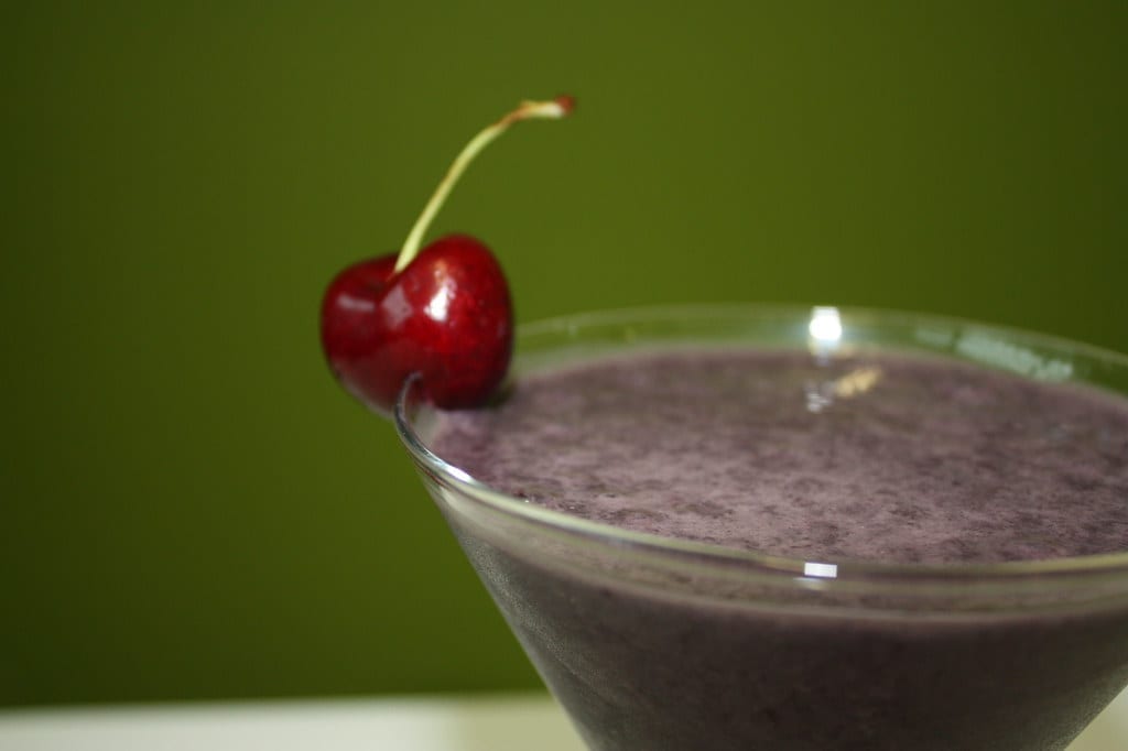 A finished purple smoothie in a glass, garnished with a fresh cherry