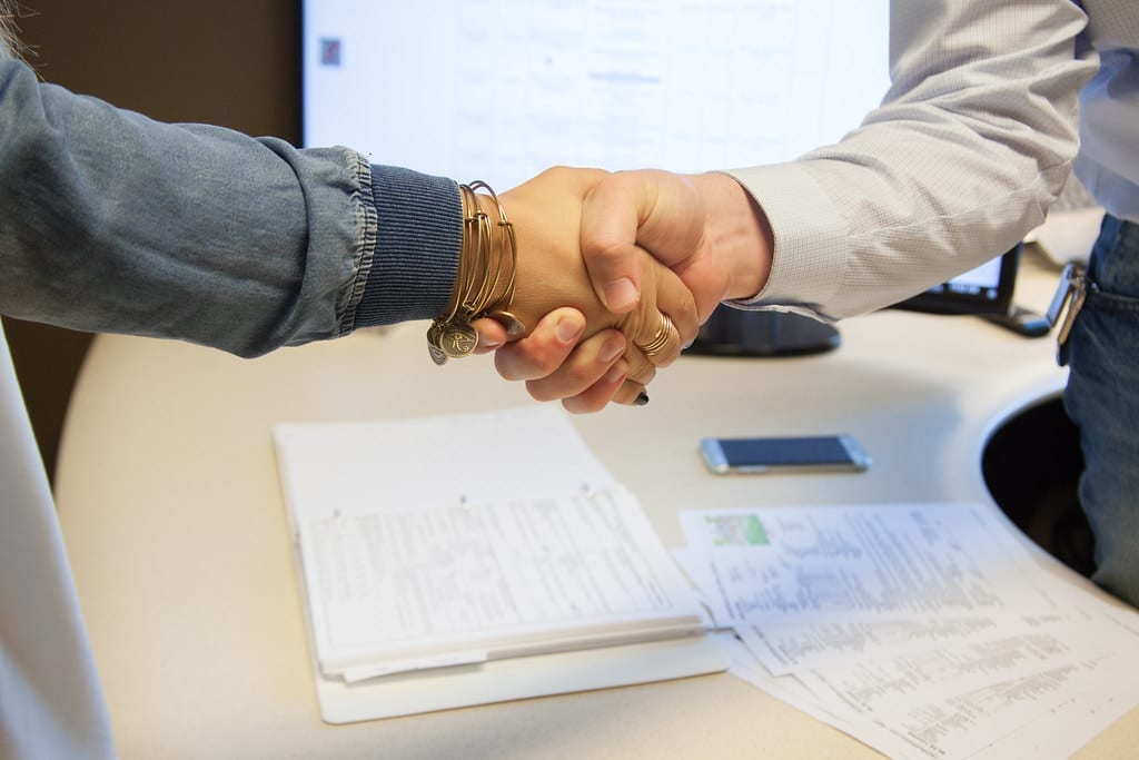 Two people shaking hands over a table with paperwork and a phone, a franchise agreement signing scene