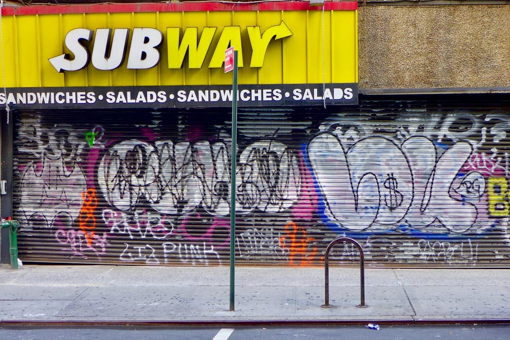 A shuttered, closed Subway storefront with its metal security gate pulled down