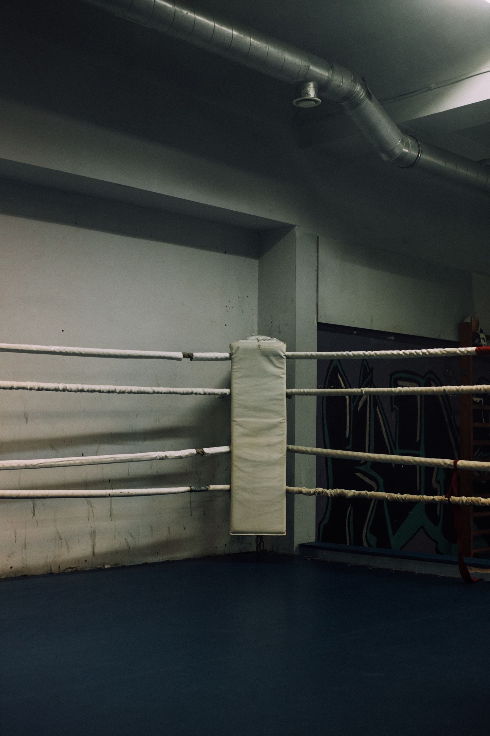 Empty boxing ring corner with wrapped ropes and a padded turnbuckle inside a combat-sports gym