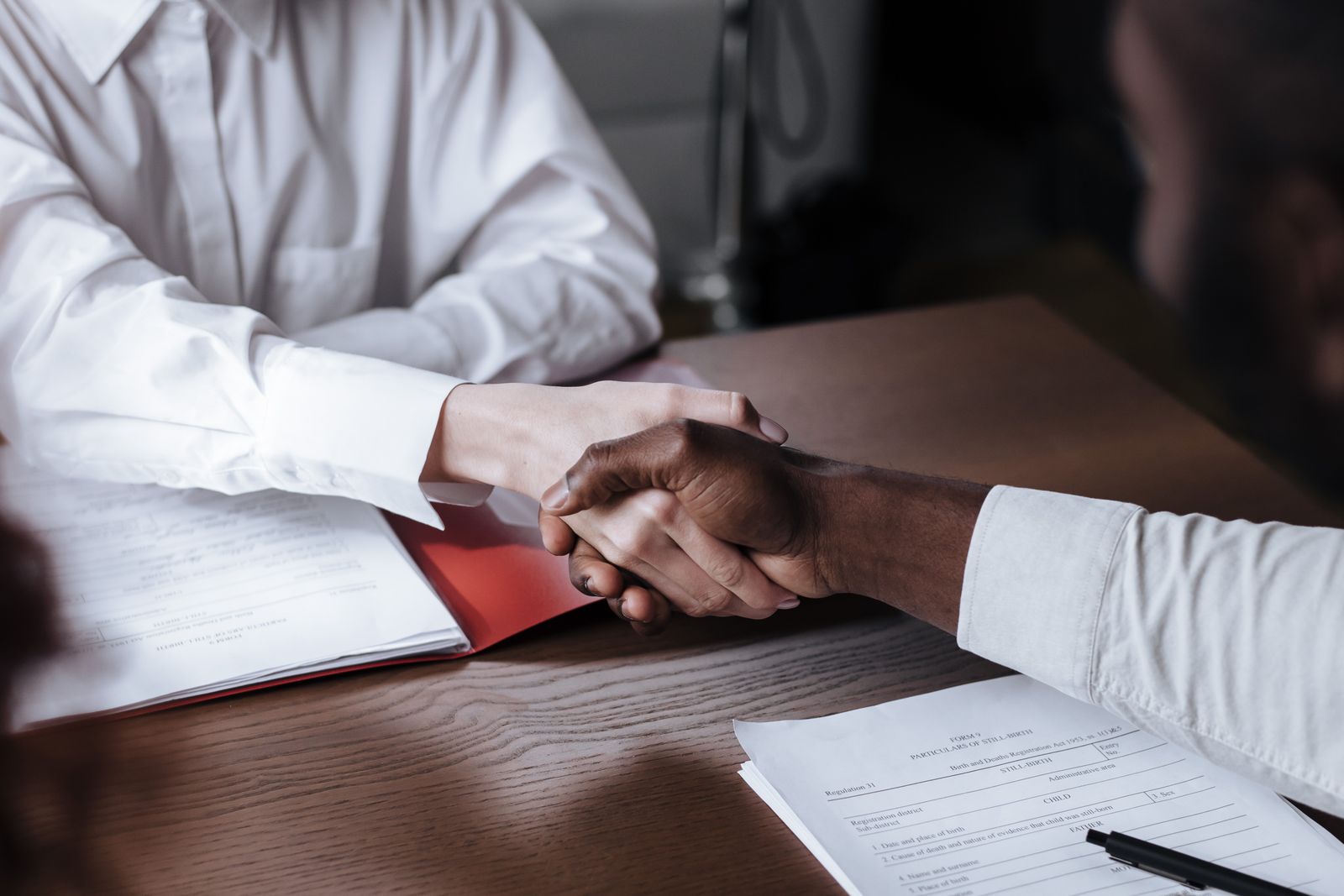 Two people shaking hands across a desk over a signed document