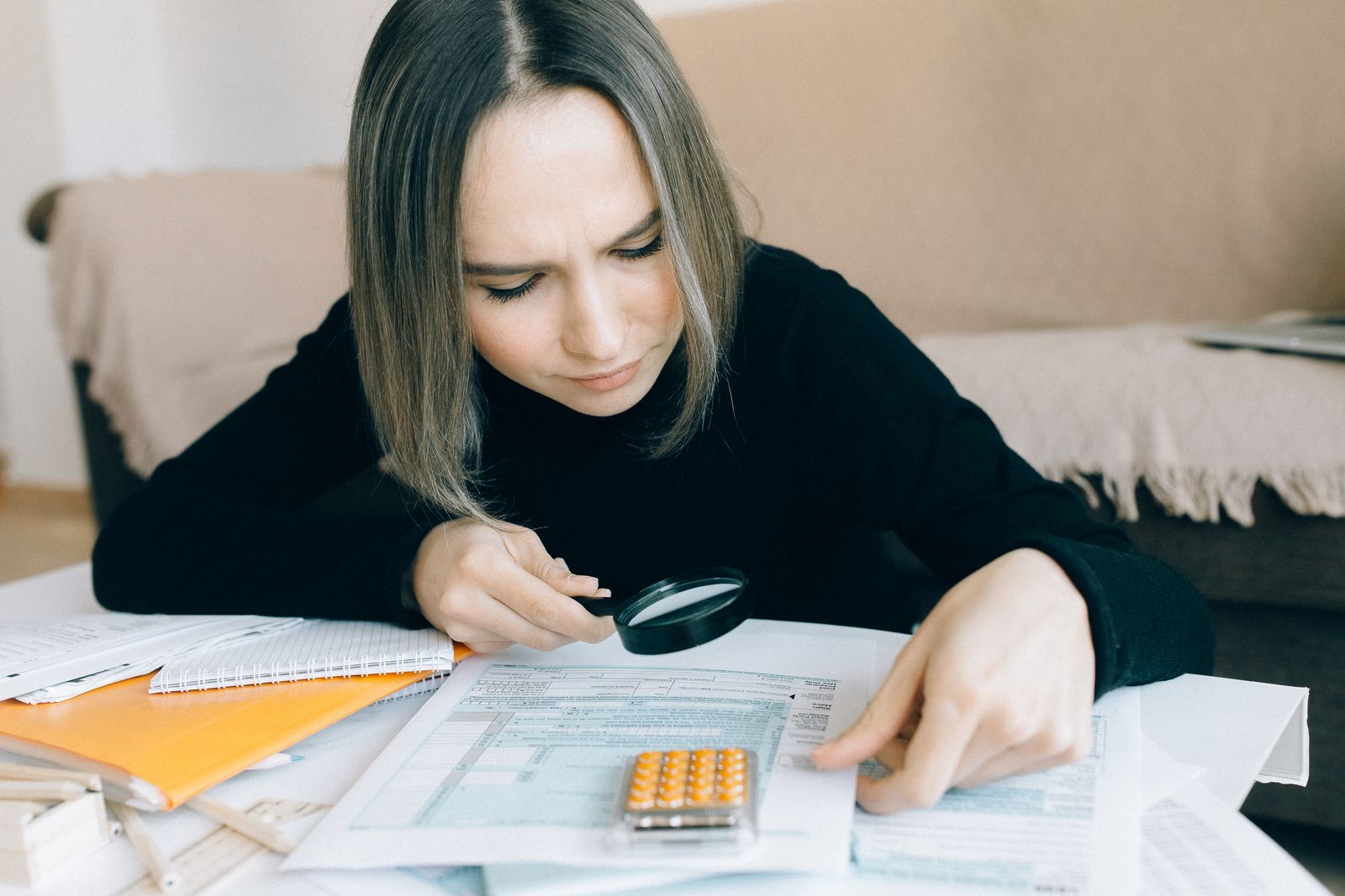 A person examining a printed form closely through a magnifying glass at a cluttered desk