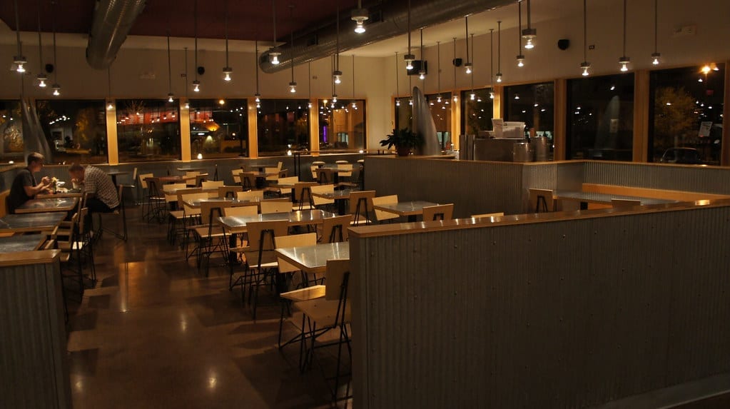 Chipotle dining room with communal tables, booth seating, and large windows, lit at night