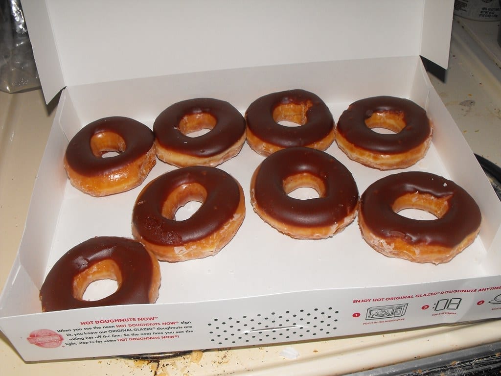 Open box of eight Krispy Kreme chocolate iced doughnuts on a branded Hot Doughnuts Now box